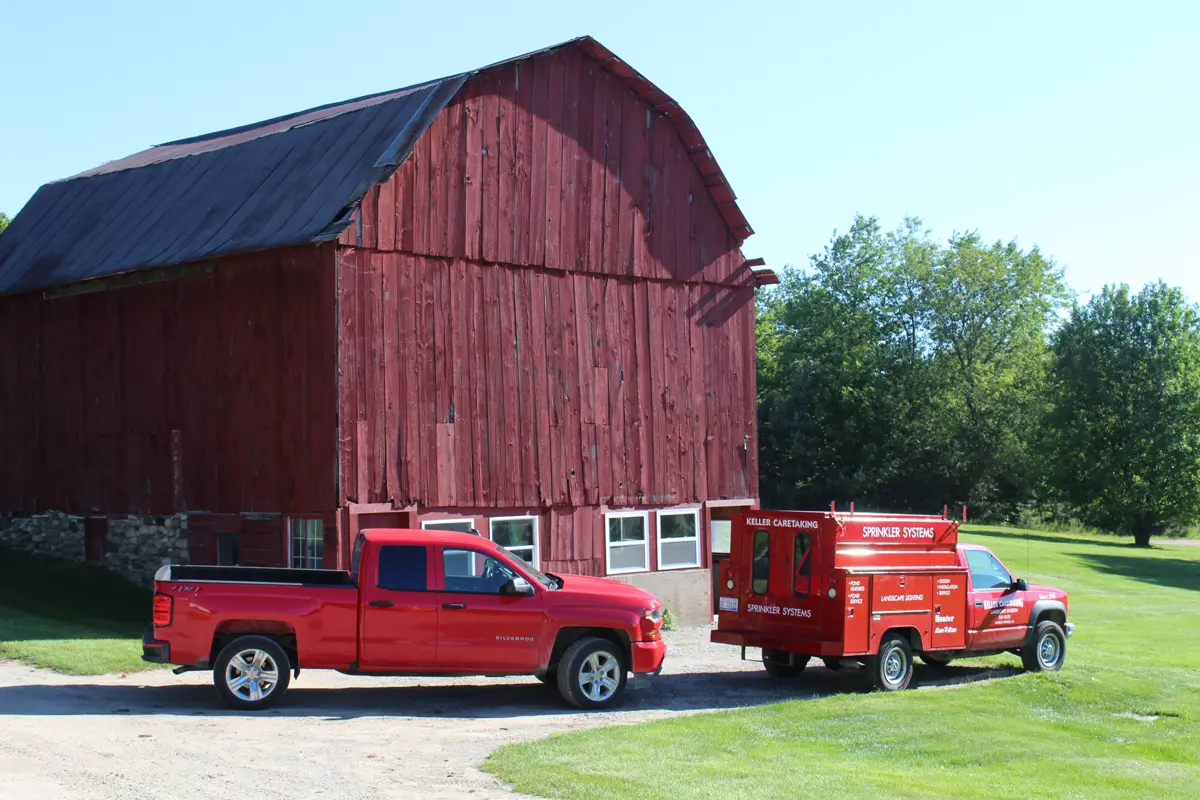 Keller Caretaking trucks parked by red barn on maintained lawn