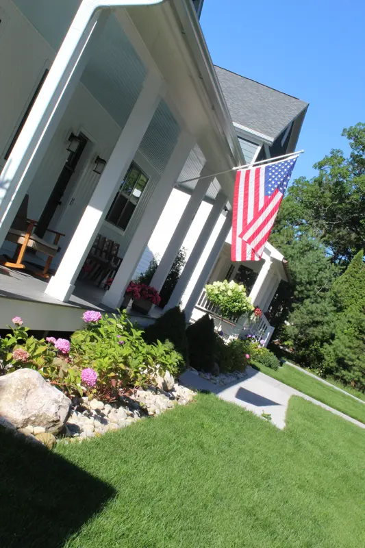 White porch with American flag and landscaped flower beds