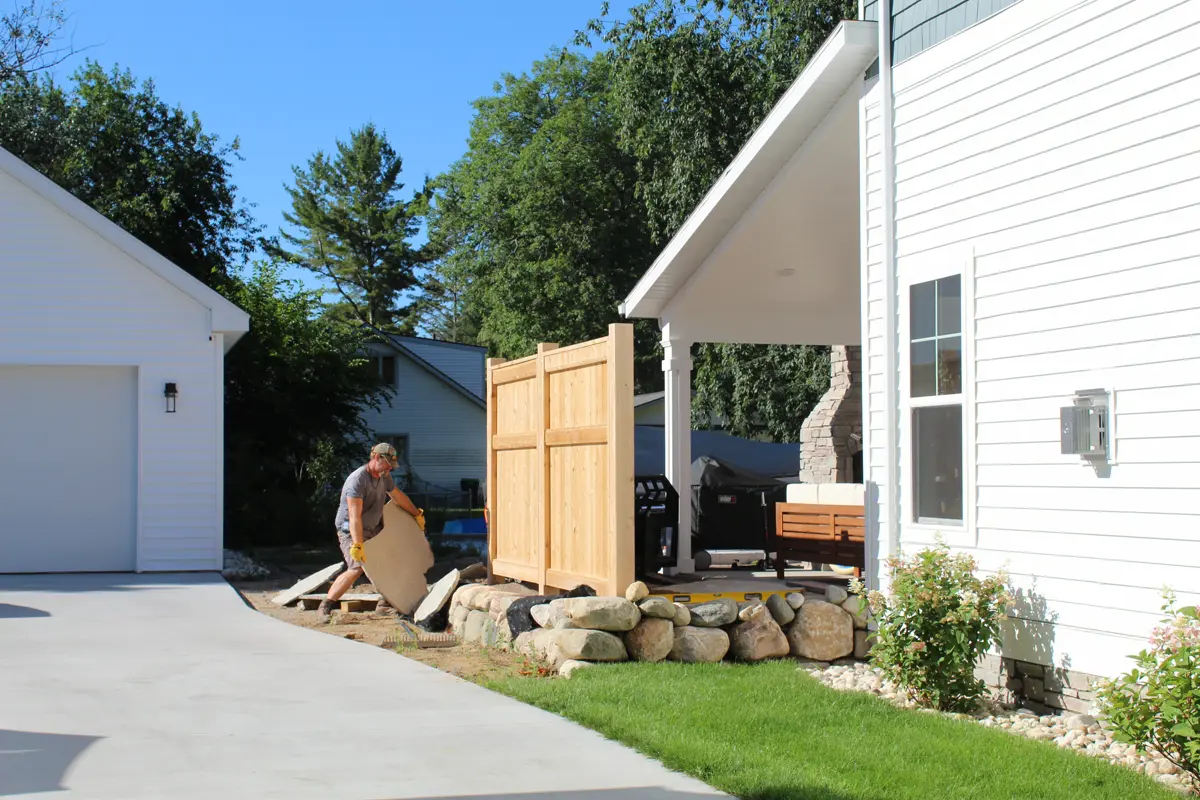 Worker installing wooden fence near stone retaining wall